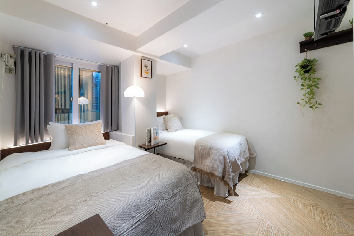 Hotelkamer met twee bedden, een groot raam met gordijnen, een tv aan de muur en een kleine plant.