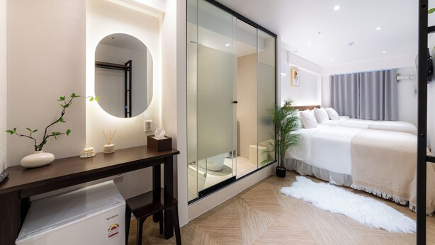 Une chambre d’hôtel moderne avec un grand lit, un bureau équipé d’un ordinateur, un miroir et une plante en pot.