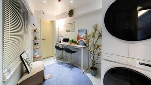 Un espace de vie compact comprenant un coin repas, un lave-linge et une plante en pot.