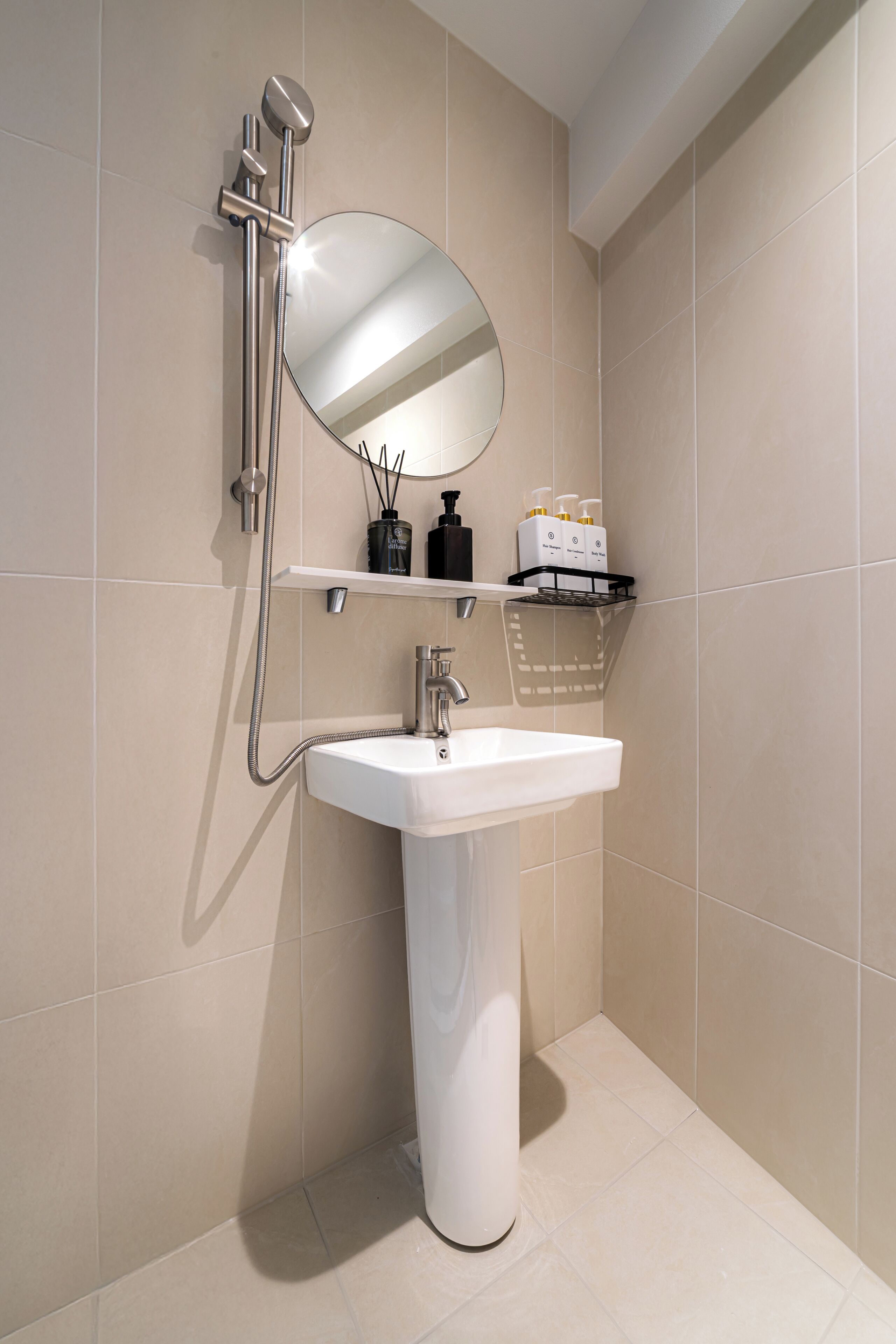 A bathroom with a white sink, a handheld showerhead, a mirror, and a shelf with toiletries.