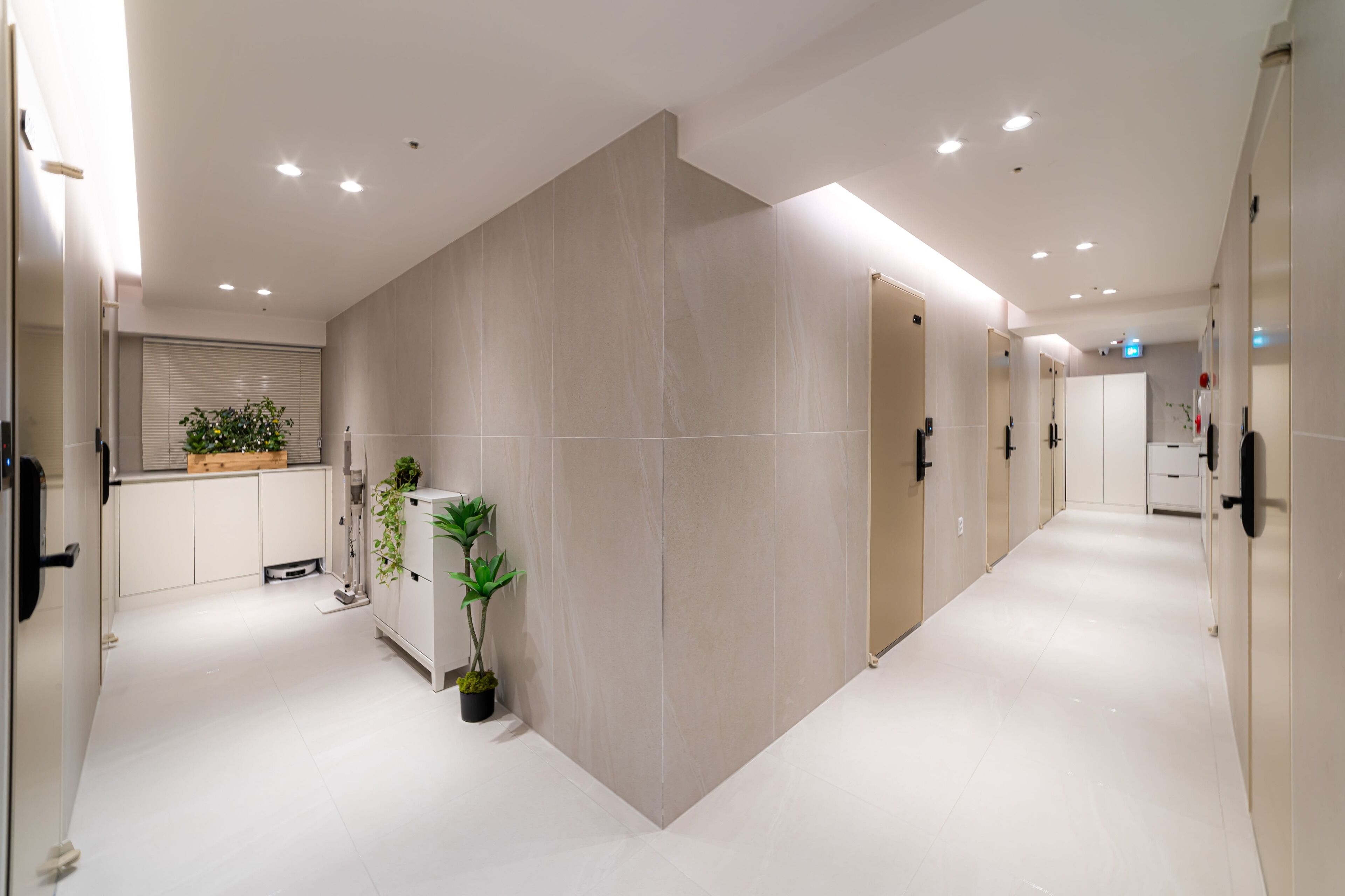 Un couloir d’hôtel moderne, au design épuré et minimaliste, avec un sol et des murs recouverts de carreaux de couleur claire, et un éclairage encastré au plafond.