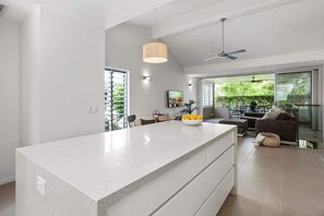 A modern kitchen with a large island, a dining area with a sofa and table, and large windows with a view of greenery.