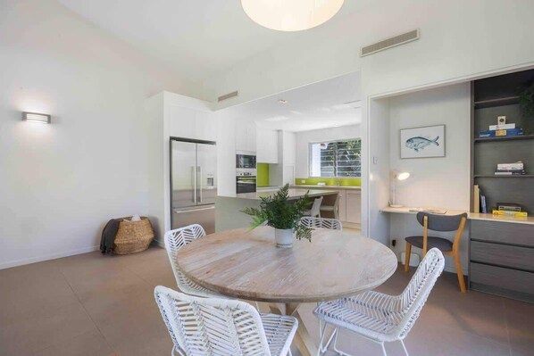A modern kitchen with white cabinets, a dining area with a round wooden table, and wicker chairs.