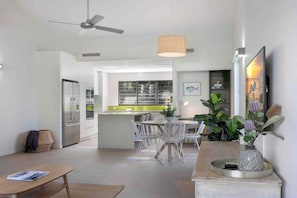 A modern kitchen with white cabinets, a dining area with white chairs, and a ceiling fan.