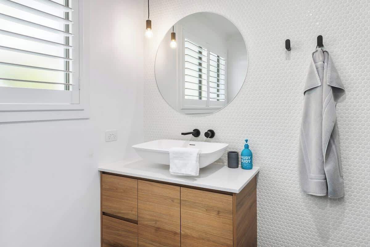 A bathroom with a white sink, wooden vanity, a round mirror, and a towel rack with a robe.