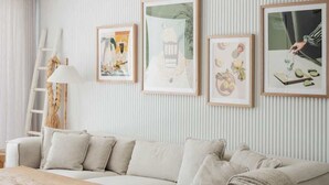 Una sala de estar con un sofá, una mesa de centro y una silla. Se observan cuadros enmarcados en la pared y un ventilador de techo.