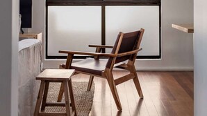 A room with a large window, a wooden chair, a small wooden table, and a television on a stand.