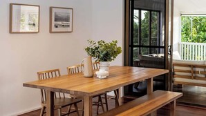 A dining area with a wooden table, benches, hanging pendant lights, framed pictures, and a view through a glass door.