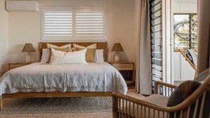 A bedroom with a bed, two bedside tables with lamps, a window with blinds, and a view of the outdoors.
