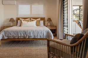 Une chambre à coucher avec un lit, deux tables de chevet avec des lampes, une fenêtre avec des stores et une vue sur l’extérieur.