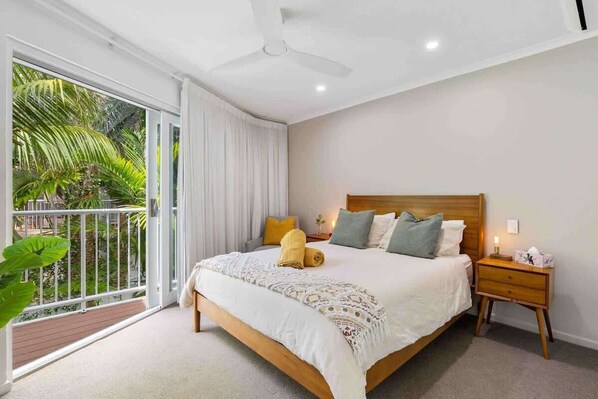 Ein Schlafzimmer mit Bett, Nachttisch und einem Balkon mit Pflanzen.