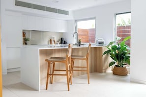 A modern kitchen with white cabinets, a wooden island, two wooden chairs, a sink, and a potted plant.