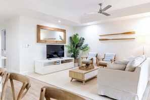 A modern living room with a flat-screen TV, a wooden coffee table, a beige sofa, and a ceiling fan. - Steps to Noosa River - a charming retreat in Noosa (Noosaville)