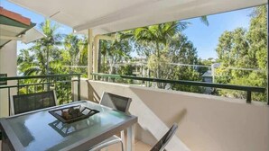 A balcony with a glass table and chairs, overlooking a tropical landscape with palm trees. - Steps to Noosa River - a charming retreat in Noosa (Noosaville)