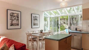 A modern kitchen with a dining area, large windows, and a red sofa. - Cute Little Cove gem…walking distance to beach! (Noosa Heads)