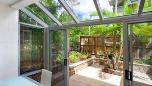 A glass-enclosed patio with a view of a wooden fence and greenery. - Cute Little Cove gem…walking distance to beach! (Noosa Heads)