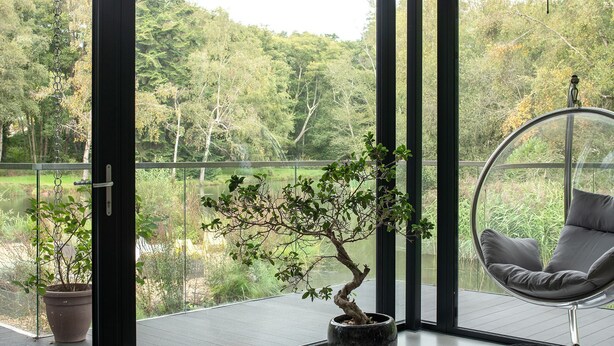 A modern room with a glass door leading to a balcony, a potted bonsai tree, and a hanging chair. - The Bridge House  -  Luxury Cottages (Bursledon)