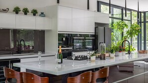 A modern kitchen with a central island, bar stools, and a large window offering a view of greenery. - The Bridge House  -  Luxury Cottages (Bursledon)