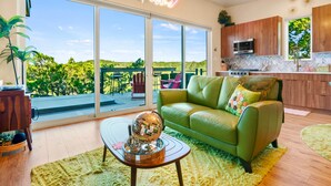 Uma sala de estar moderna com um sofá de couro verde, uma bola de espelhos e uma grande porta de vidro deslizante que dá para uma varanda com vista para o verde.