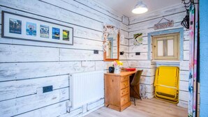 A room with white wooden walls, a wooden dresser, a mirror, a radiator, and a yellow chair. - The Studio At Raymond House - Penally - Tenby (Tenby)