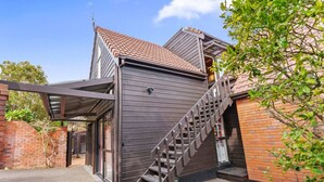 Una moderna casa a due piani con facciata in legno, un portico coperto e una scala che conduce al piano superiore.