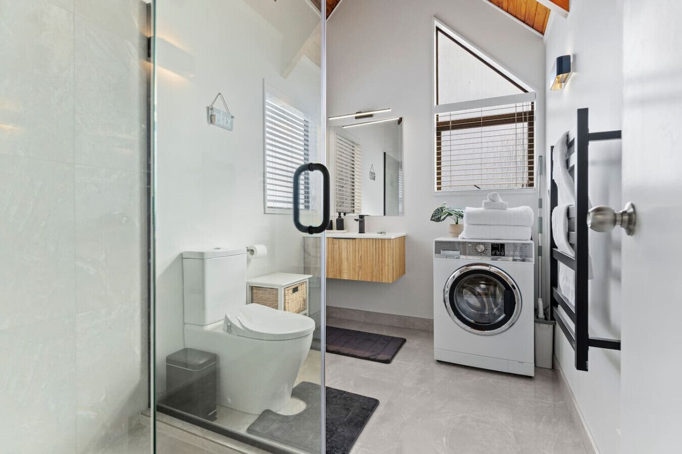 A modern bathroom with a glass shower enclosure, a toilet, a sink, and a washing machine.