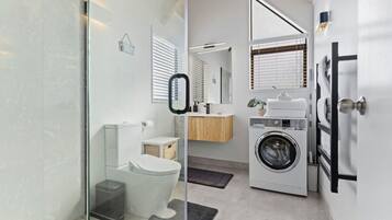 A modern bathroom with a glass shower enclosure, a toilet, a sink, and a washing machine.
