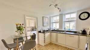 Una cocina moderna con armarios blancos, una mesa de comedor de cristal y piso de madera.