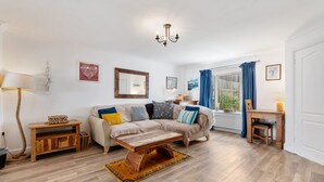 Un salon comprenant un canapé, une table basse, une table d’appoint en bois et une fenêtre avec des rideaux.