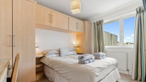 Une chambre à coucher avec un lit, des lampes de chevet, une fenêtre avec des rideaux et des armoires en bois.
