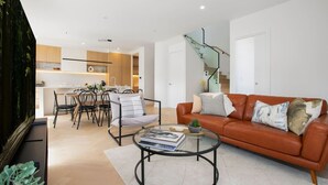 Uma sala de estar moderna com um sofá de couro, uma mesa de centro de vidro e uma área de jantar com mesa e cadeiras de madeira.