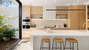 Uma cozinha moderna com uma ilha central, banquetas de bar, eletrodomésticos embutidos e vista para o exterior.