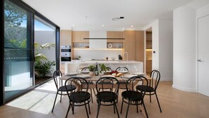 Cozinha moderna com ilha central, área de jantar com cadeiras e uma grande porta de vidro deslizante para um jardim.