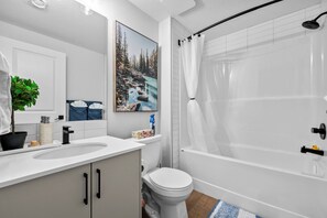 Une salle de bain moderne avec un lavabo, des toilettes et une baignoire, le tout de couleur blanche. Une grande fenêtre offre une vue sur une forêt et une rivière.