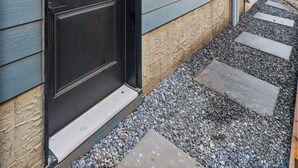 A modern building with a black door, a small window, and a pathway leading to the entrance.