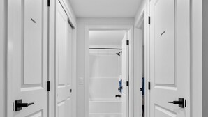 A hallway with white doors and a wooden floor, leading to a bathroom with a shower and a toilet.