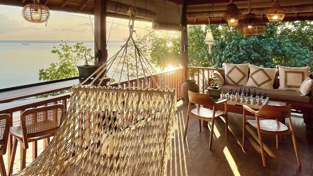 A hammock chair, wooden deck chairs, a chess table, and a sofa with patterned cushions. - Nico's House (Lembongan Island)