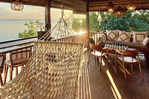 A hammock chair, wooden deck chairs, a chess table, and a sofa with patterned cushions. - Nico's House (Lembongan Island)