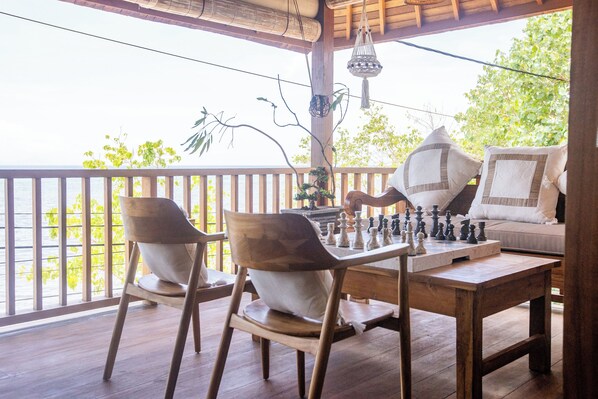 A wooden deck with a chessboard, two chairs, and a sofa with cushions. - Nico's House (Lembongan Island)