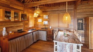 A rustic wooden interior with a kitchen area, wooden ceiling beams, and pendant lighting. - Nico's House (Lembongan Island)