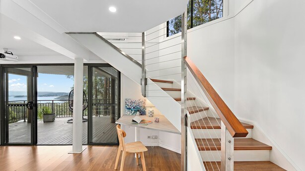 A modern interior with a wooden floor, a desk with a chair, a staircase with wooden steps, and a view through glass doors to an outdoor deck.