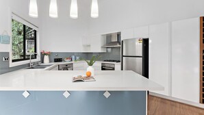 A modern kitchen with white cabinetry, a central island, pendant lighting, and a view of greenery outside.