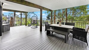 A covered outdoor deck with a table and chairs, overlooking a body of water and trees.