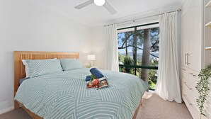 A bedroom with a bed, a ceiling fan, a window with curtains, and a view of trees and mountains.