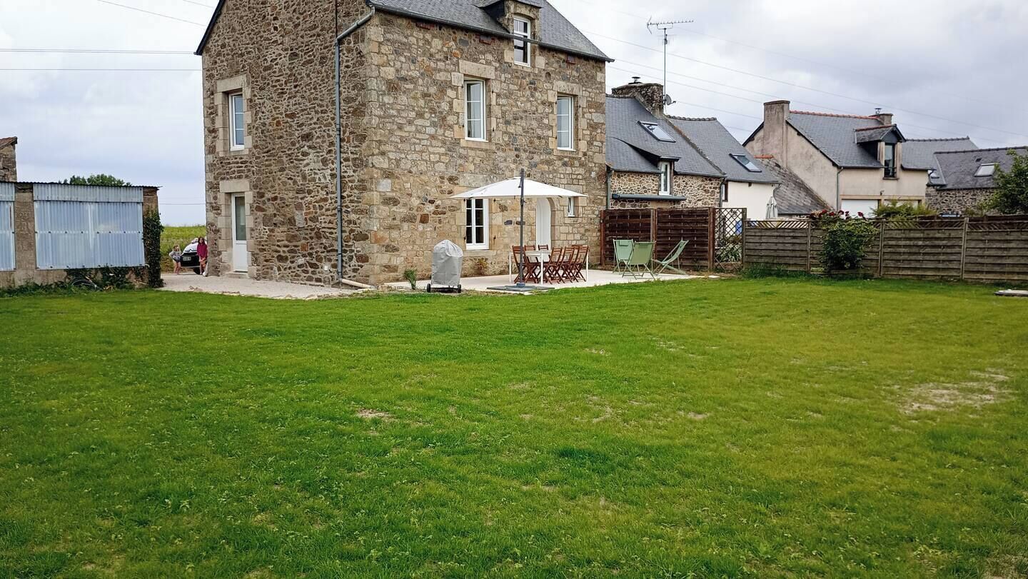 Une maison en pierre avec une cour verdoyante, un espace extérieur aménagé pour s’asseoir et un coin barbecue couvert.