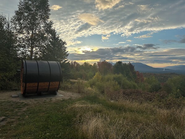 A rustic wooden barrel in a natural setting with a view of mountains and a cloudy sky.