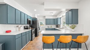 Una cucina moderna con mobili color petrolio, un'isola centrale con sgabelli da bar e un frigorifero in acciaio inossidabile.