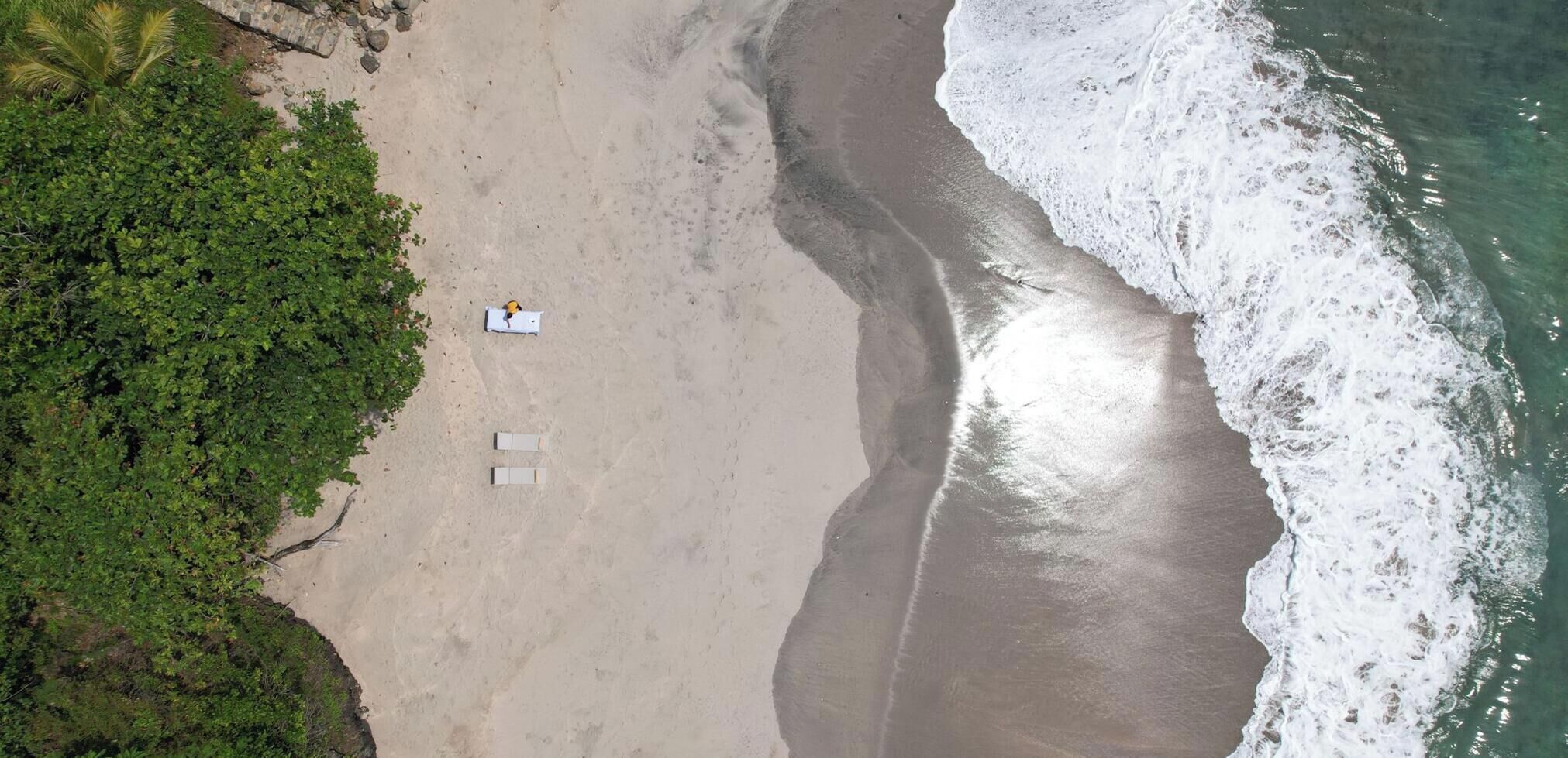 An aerial view of a beach with a few lounge chairs and a person lying on a towel.