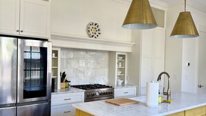 Una cucina moderna con frigorifero in acciaio inossidabile, piano cottura a gas e zoccolo di marmo. Due lampade a sospensione illuminano l'isola, e ci sono un set di sgabelli da bar.