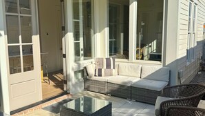 Una veranda riparata con mobili in vimini, un tavolino in vetro e una ventola a soffitto.